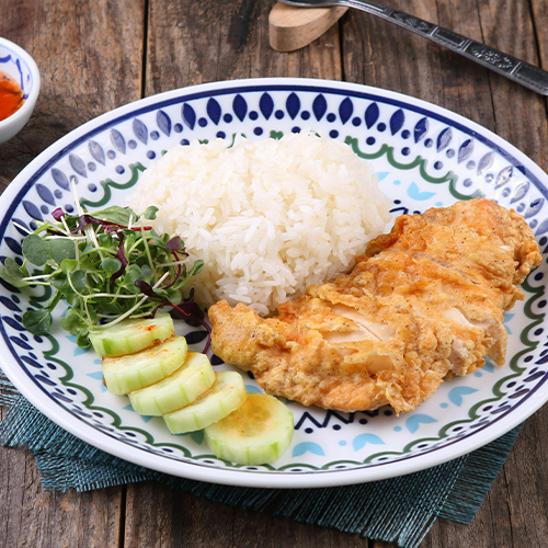 Prato com arroz branco, filé de frango grelhado, rodelas de pepino e mix de folhas, servido sobre mesa de madeira.