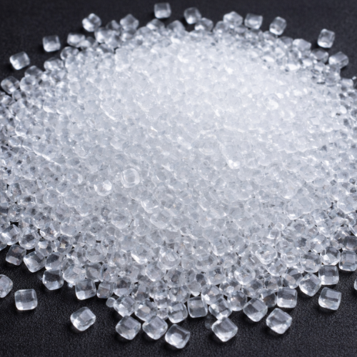 Grânulos transparentes e pequenos de material plástico dispostos sobre superfície escura em close.